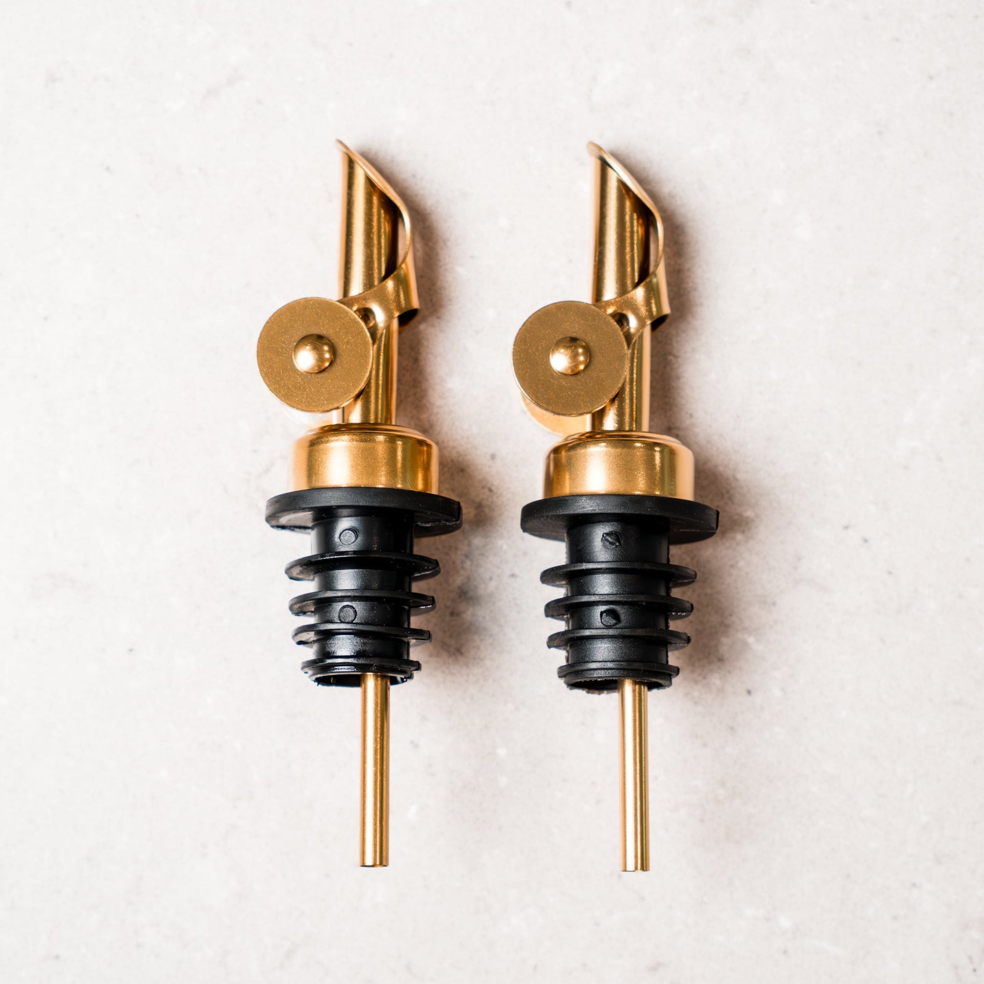 Two gold and black bottle spouts on a light gray background